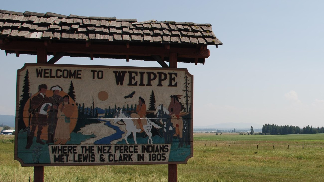 A grassy meadow with traditional Nez Perce structures at dawn.